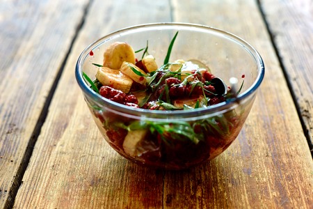 salad of fresh bananas, raspberries, estragon and honey in transparent plate on wooden background. Selective focusの写真素材