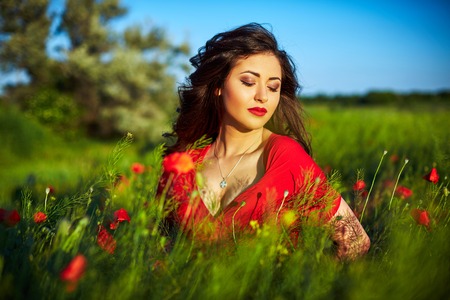 Beautiful woman in a poppy field with flowers. Woman wearing in a red dress.の写真素材