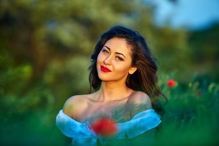 Beautiful woman in a poppy field with flowers. Woman wearing in a white dress.の写真素材