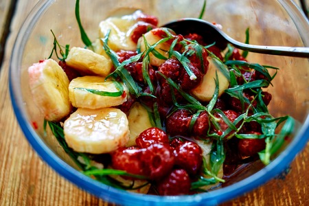 salad of fresh bananas, raspberries, estragon and honey in transparent plate on wooden background. Selective focusの写真素材