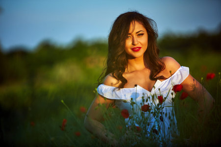 Beautiful woman in a poppy field with flowers. Woman wearing in a white dress.の写真素材