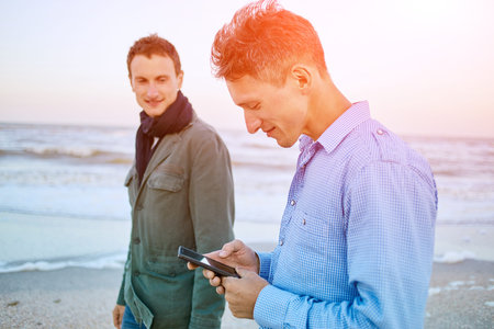 two friends on the beach at the  sunset. one man holding smartphoneの写真素材