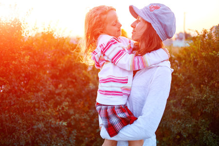 attractive family, woman and girl  against green bushes at the sunset
