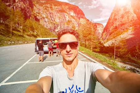 young  man make selfie on the morning mountains background. Man dressed in a white t-shirt and white sunglassesの写真素材