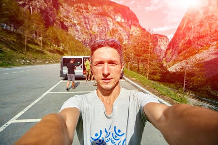 young  man make selfie on the morning mountains background. Man dressed in a white t-shirt and white sunglassesの写真素材
