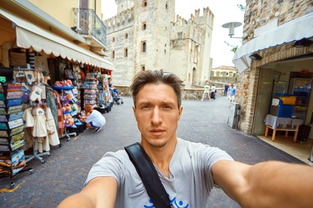 young  man make selfie on the old italian town background. Man dressed in a white t-shirt and white sunglassesの写真素材