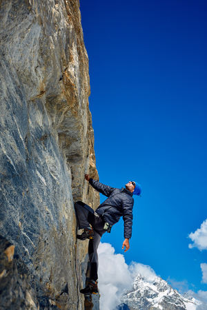 Young man climbs on a rocky wall, against a blue skyの写真素材