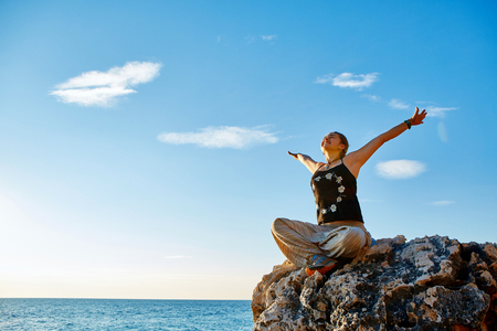 young woman with  dreadlocks sitting in the lotus position on the cliff against sea and blue sky at early morningの写真素材