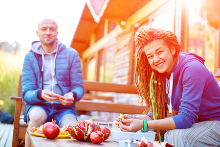 man and young woman with  dreadlocks in the garden on the veranda of the house eating pomegranatesの写真素材