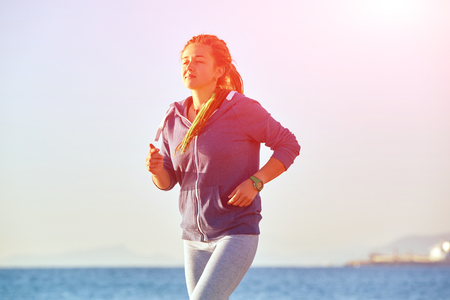 young woman running on the beach against sea and blue sky at early morningの写真素材