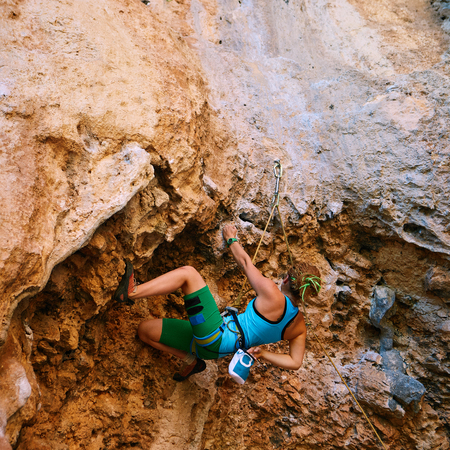 female rock climber climbs on a rocky wall. climbs through the overhanging portionの写真素材