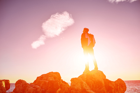traveler with backpack standing on the cliff against sea and blue sky at early morningの写真素材