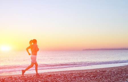 young woman running on the beach against sea and blue sky at the sunriseの写真素材