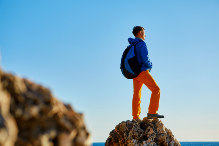 traveler with backpack standing on the cliff against sea and blue sky at early morningの写真素材