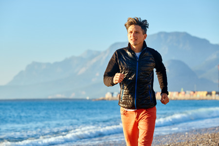 young man running on the beach against sea and blue sky at early morningの写真素材