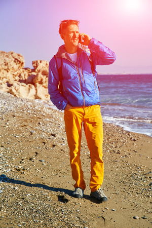 young man standing on the beach against sea and blue sky at early morning and talking by the phoneの写真素材