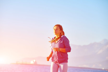 young woman running on the beach against sea and blue sky at early morningの写真素材