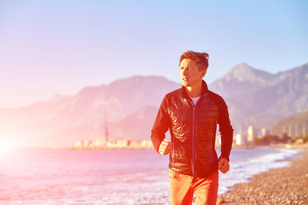 young man running on the beach against sea and blue sky at early morningの写真素材