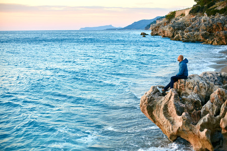 man sitting on the cliff on the beach against the sea  at early morningの写真素材