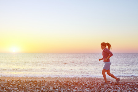 young woman running on the beach against sea and blue sky at the sunriseの写真素材