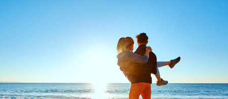 happy attractive man and woman walking on the sunny beach over the blue sky. man holding a woman on the hands.の写真素材
