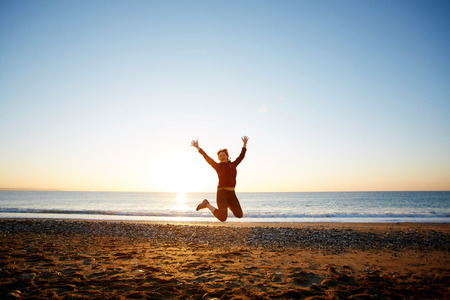 young woman jumping on the beach against sea and blue sky at the sunriseの写真素材