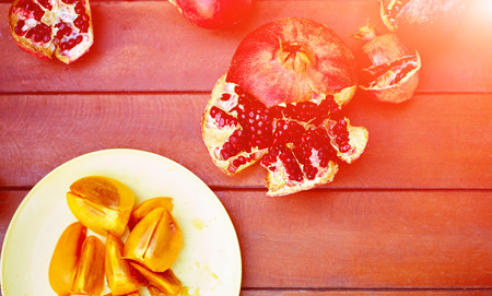 Sliced persimmon fruit and ripe cracked raw pomegranates on a dark wooden backgroundの写真素材