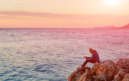 young man on the beach against sea and sunrise sun at early morning and looks at the phoneの写真素材