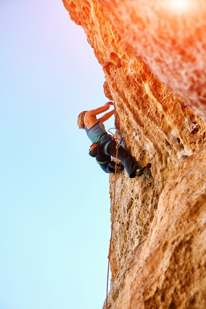 female rock climber climbs on a rocky wall against a blue skyの写真素材