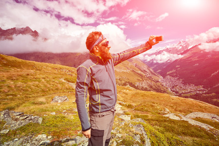 hiker at the top of a pass  enjoy sunny day in Alps and take photo on smartphone. Switzerland, Trek near Matterhorn mount.の写真素材