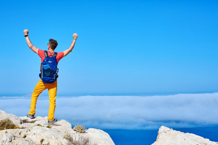traveler with backpack standing on the cliff against sea and blue sky at early morning