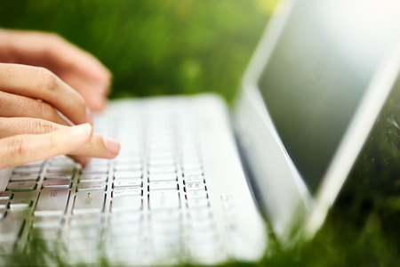 young woman with laptop lying on the grass in the park. palm and laptop closeupの写真素材