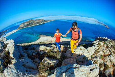 couple of  travelers with backpack standing on the trail against sea and blue sky at early morning. Balos beach on background, Crete, Greeceの写真素材