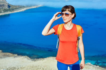 female traveler with backpack  standing on the trail against sea and blue sky at early morningの写真素材