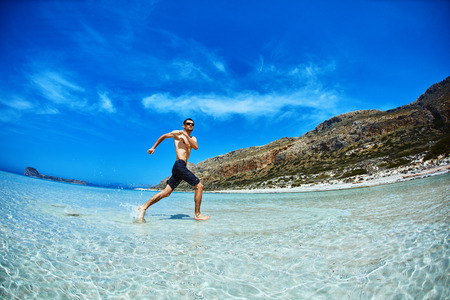 strong athletic man  with bared torso running on the beach along the sea frontの写真素材