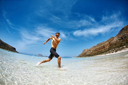 strong athletic man  with bared torso running on the beach along the sea frontの写真素材