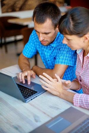 young man and woman with laptop typing on the keyboard in cafe.