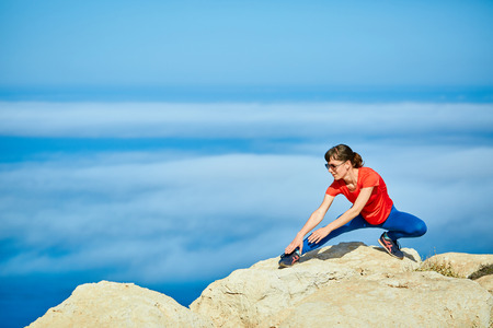 young woman doing sports workout on the cliff against sea and blue sky at early morningの写真素材