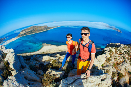 couple of travelers with backpack standing on the trail against sea and blue sky at early morning. Balos beach on background, Crete, Greeceの写真素材