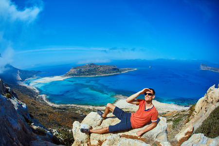 man relaxing on a rock against a blue seaの写真素材