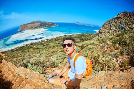 male traveler with backpack sitting on the trail against sea and blue sky at early morning.の写真素材