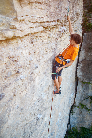male rock climber. rock climber climbs on a rocky wall. climber threading the rope in quickdrawの写真素材