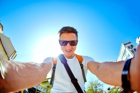 man tourist makes selfie in the city in the summer on a background of blue skyの写真素材