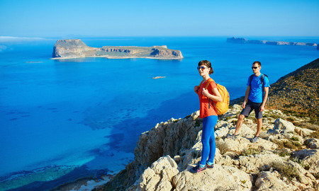 couple of travelers with backpack standing on the cliff against sea and blue sky at early morning. Balos beach on background, Crete, Greeceの写真素材