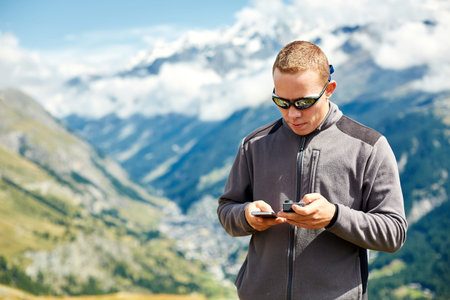 hiker at the top of a pass with smartphone and action camera enjoy sunny day in Alps. Switzerland,...