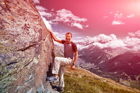 Adult man climbs on a big stone, against a blue sky and valley with Zermatt townの写真素材
