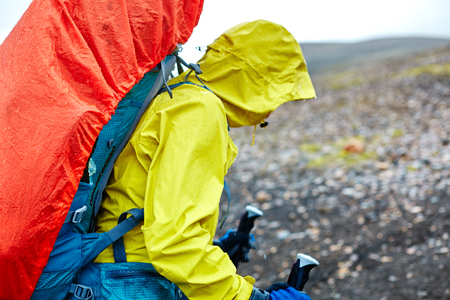 woman hiker on the trail in the Islandic mountains. Trek in National Park Landmannalaugar, Iceland. woman walking in the rain with a backpack in a raincoat and wearing a waterproof jacketの写真素材