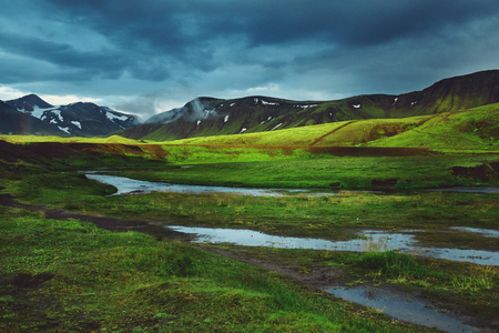 Travel to Iceland. Beautiful sunset in camping near Alftavatn lake. Icelandic landscape with mountains, sky and clouds. Trekking in national park Landmannalaugar. Rainy Evening with big rainbow.の写真素材