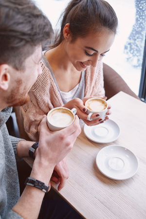 Couple on a date at a cafe drinking coffee by the window . smiling woman looking at the man with love.の写真素材
