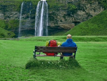 famous Skogarfoss waterfall in southern Iceland. The traveler sits on a bench and looks at the waterfall. treking in Iceland. Travel and landscape photography conceptの写真素材